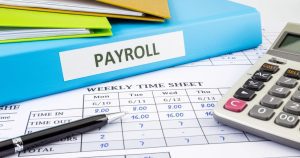Payroll file, calculator, and weekly timesheet on office desk