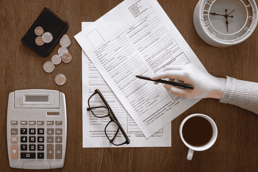 A person filling out an application form with a pen, calculator, and coffee on a desk