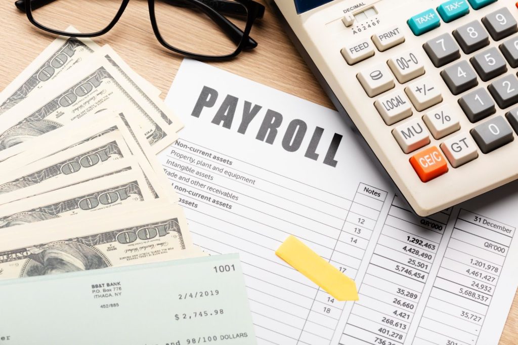 A desk with a calculator, a payroll document, and a pen