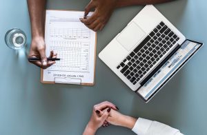 Two people meeting at a desk with a daily report schedule.