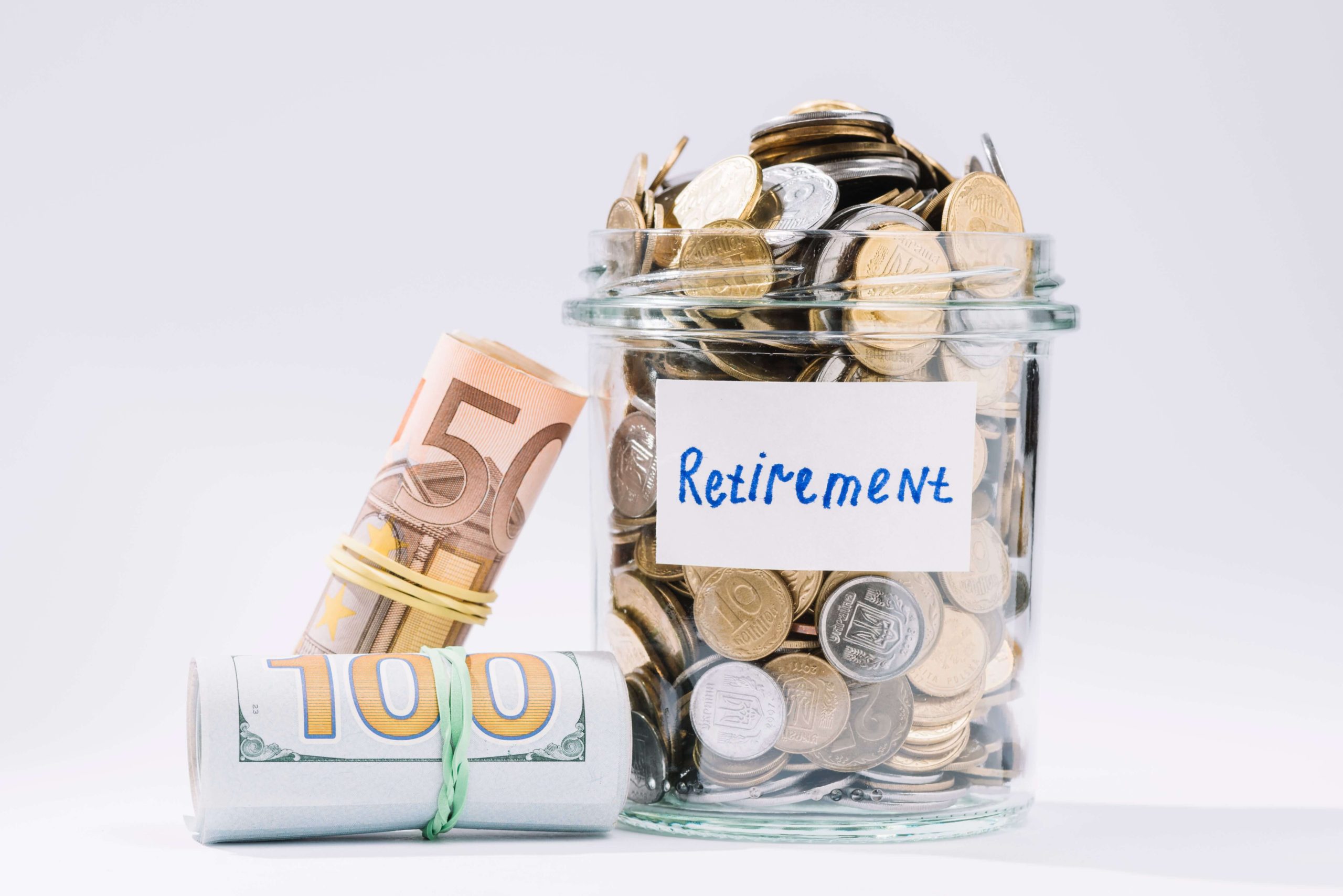 Glass jar labeled Retirement filled with coins alongside rolled banknotes, representing financial planning, savings, and investment for retirement.