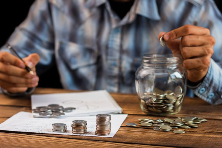 Person counting coins and saving money in a jar.