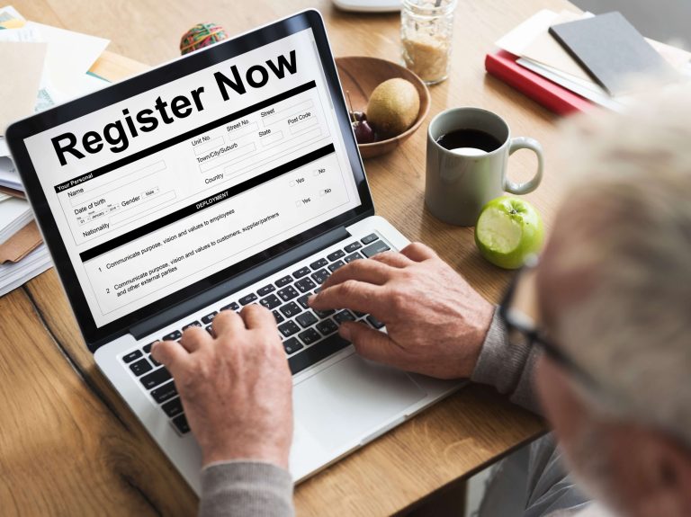 A person typing on a laptop with a "Register Now" form on the screen