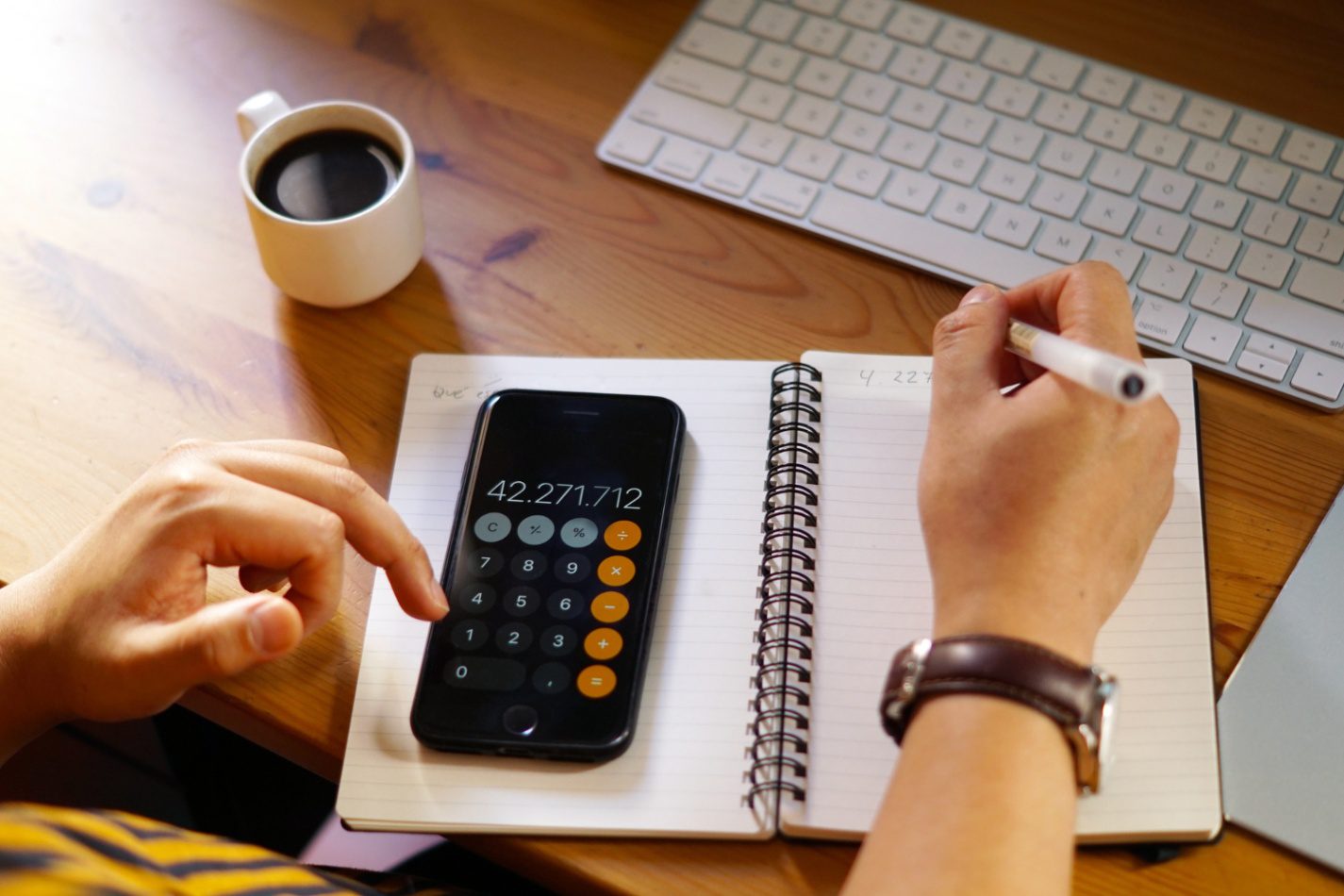 Person calculating weekly pay on smartphone calculator while writing notes at desk